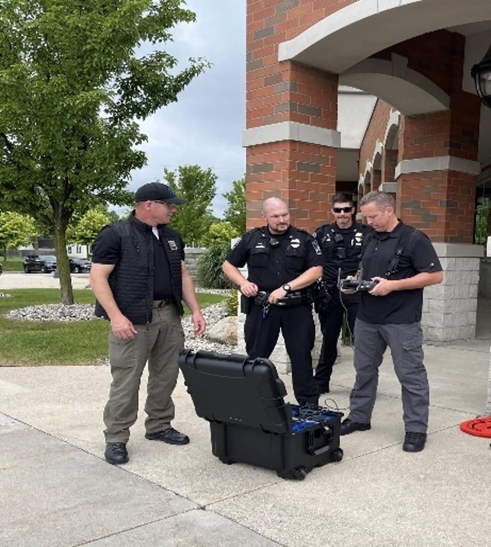 Four men standing with black box containing drone in front of them